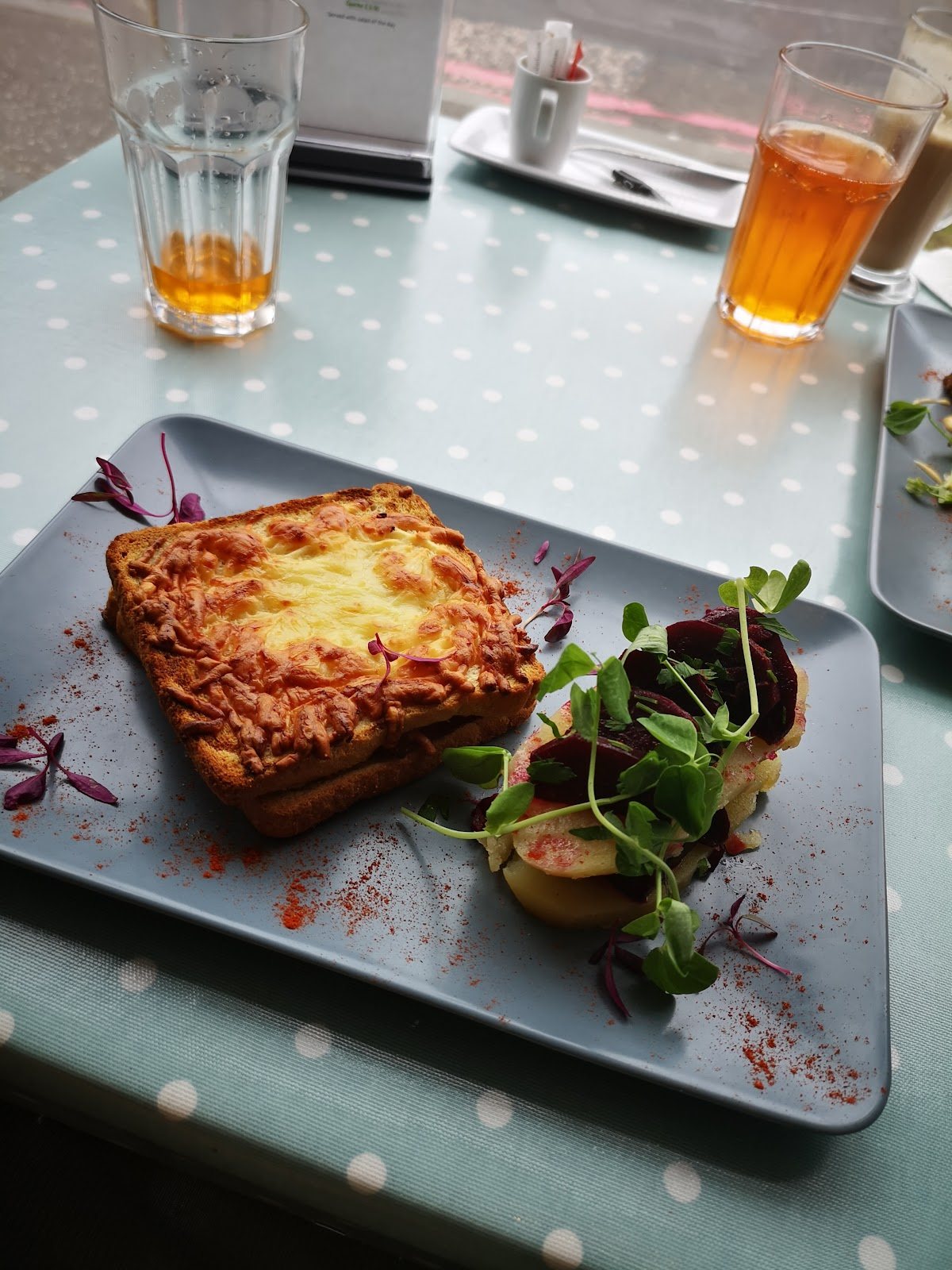 A golden, grilled cheese-topped toastie with a beetroot, potato and pea-shoot salad, on a grey plate on the polka-dot tablecloth.