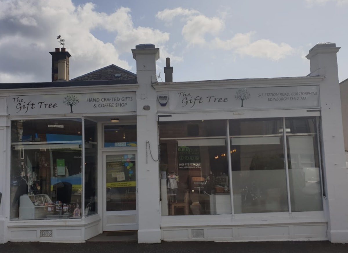 The Gift Tree's white-painted double shopfront on Station Road, with two fascia signs carrying a tree logo: 'Hand crafted gifts & coffee shop' and '5-7 Station Road, Corstorphine, Edinburgh EH12 7AA'.