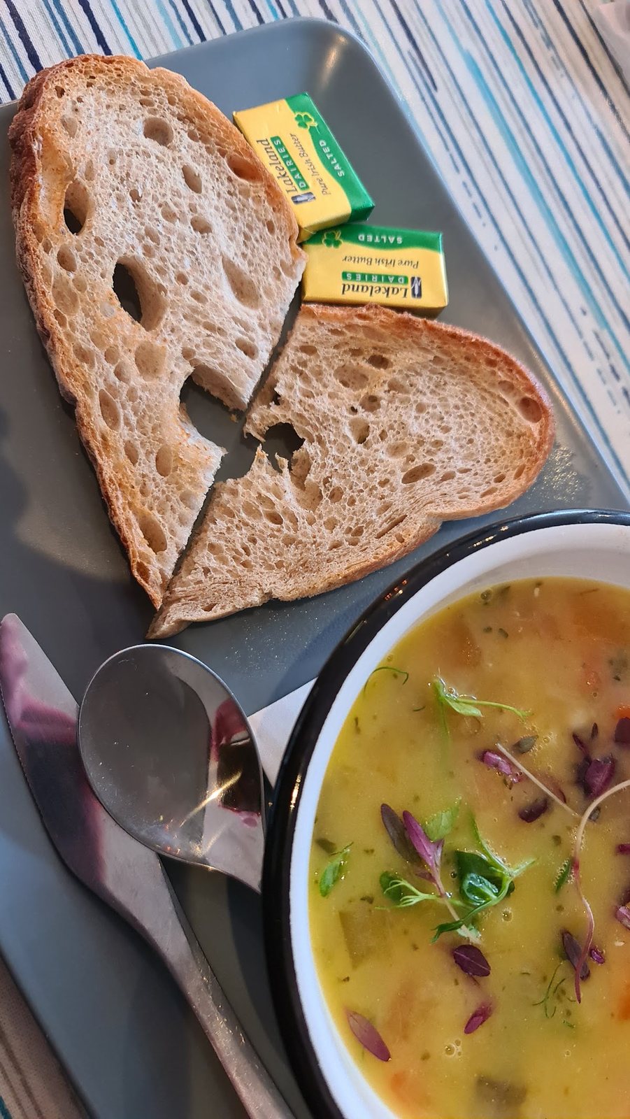 A bowl of vegetable soup topped with micro herbs, with two slices of sourdough and butter.