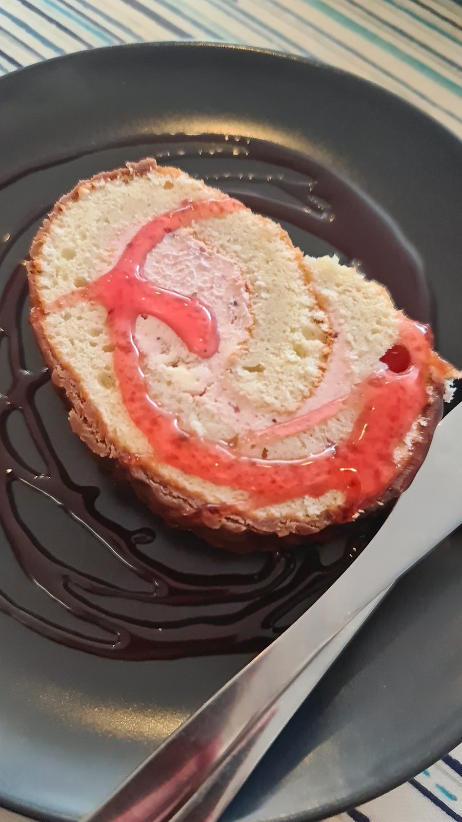 A slice of Swiss roll swirled with raspberry jam on a plate with a chocolate drizzle.